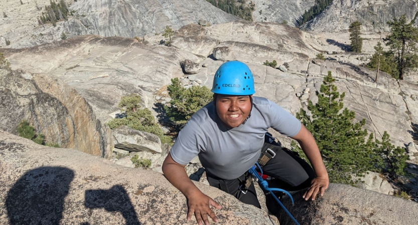 a person wearing a helmet smiles during a rock climbing trip for bipoc